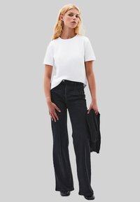 Un jean évasé noir associé à un t-shirt à manches courtes blanc. Le t-shirt a un col rond, et le jean présente des poches avant et des détails de couture.
