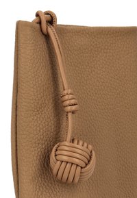 Bruine leren handtas met een getextureerde afwerking, voorzien van een detail met een geknoopte handgreep. De tas heeft een gestructureerde vorm en gladde accenten.