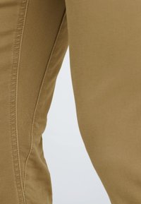 Beige cotton pants with a smooth texture, featuring side seams and a fitted design. Visible stitching adds detail to the fabric.