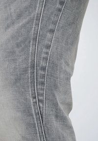 Vaqueros gris claros con un acabado texturizado, que presentan un primer plano de la tela y las costuras, mostrando un ligero desgaste y un diseño ajustado.