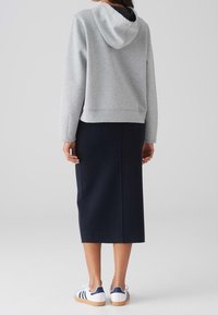 Sweat à capuche gris avec une doublure noire, jupe crayon bleu marine et chaussures blanches avec des rayures bleues. Tenue décontractée mettant en valeur des tissus doux et des lignes épurées.