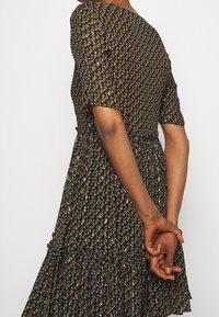 Musta mekko, jossa on pieni kukkakuosi, lyhyet hihat, kerätty vyötärö ja kerroksellinen röyhelöhelma. Kankaan ilme on kevyt ja tekstuuri.