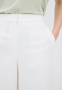Witte op maat gemaakte broek met een gladde textuur, voorzien van zijzakken en een strakke, minimalistische uitstraling. De tailleband is plat en gestructureerd.