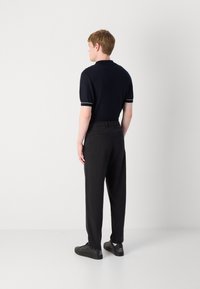 Polo shirt bleu marine à manches courtes avec des accents blancs, associé à un pantalon noir. Le modèle porte des baskets noires. Design simple et moderne.