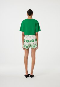 Groene, korte mouwen, cropped T-shirt gecombineerd met witte scalloped shorts met groene bloemmotieven en decoratieve accenten. Zwarte hakken.