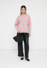 Roze en grijsgestructureerde gebreide trui met een ronde hals, gecombineerd met zwarte nep leren wijde broek en een kleine zwarte handtas.