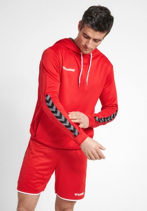 Rode sportieve hoodie met grijze chevronpatroon op de mouwen en bijpassende rode shorts. De stof lijkt lichtgewicht en ademend te zijn met een capuchon met trekdraad.