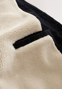Tissu polaire couleur crème avec une texture douce à côté d'une poche en velours côtelé noir sur un vêtement.