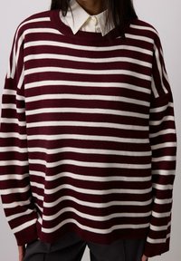 Maglione a righe bordeaux e bianche con scollatura rotonda e vestibilità ampia. Tessuto a maglia, maniche lunghe, con una camicia bianca a contrasto sotto.