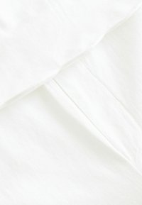 Tissu blanc avec une texture lisse, présentant de légers plis et un détail de couture, indiquant une douceur et une construction légère.