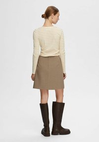 Maglietta a maniche lunghe a righe crema e beige abbinata a una gonna beige e stivali di pelle marrone scuro fino al ginocchio. Tessuto morbido e design semplice.