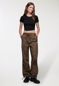 T-shirt nera tagliata abbinata a pantaloni cargo larghi color verde oliva con un motivo a corteccia d'albero, vita con cordoncino e tasche laterali. Stivali neri robusti.