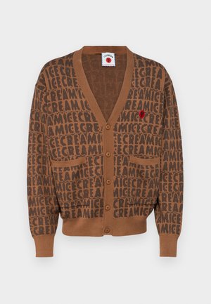 Pruun kardigan, millel on korduv "JÄÄTIS" muster. Sellel on V-kaelus, nööbiga kinnitamine ja kaks esmost taskut. Kaunistav punane embleem on kaasas.