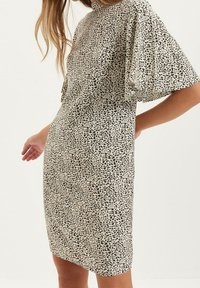 Vestido de manga corta en tejido crema con un patrón de estampado animal negro. El diseño es entallado con un escote alto y una textura sutil.