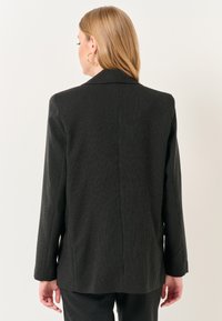Blazer nero a righe con una texture liscia, dotato di un colletto strutturato, maniche lunghe e una linea dritta. Design minimalista.