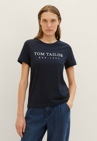T-shirt marine à manches courtes, arborant le texte imprimé en blanc "TOM TAILOR EST. 1962" sur le devant, fabriqué en coton doux.