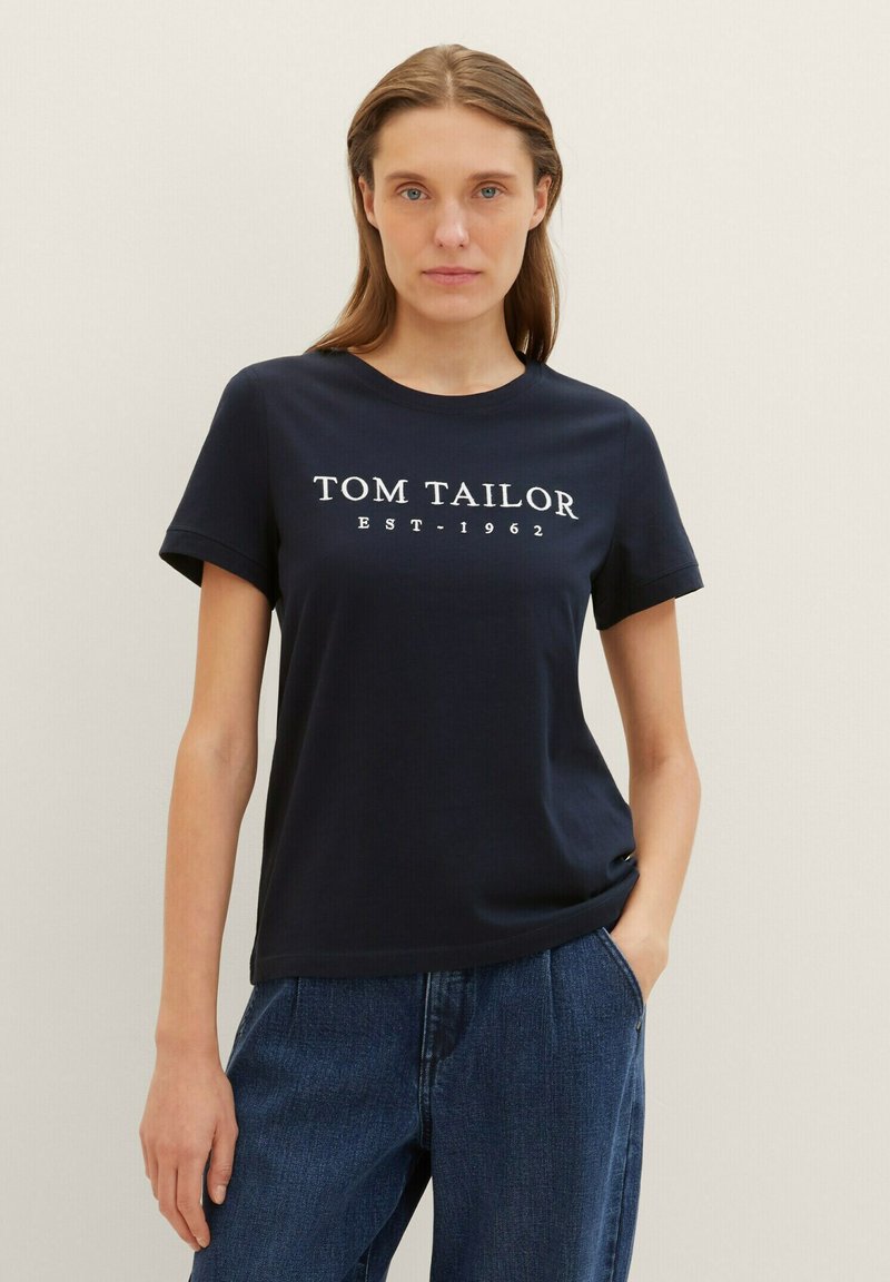 T-shirt marine à manches courtes, arborant le texte imprimé en blanc "TOM TAILOR EST. 1962" sur le devant, fabriqué en coton doux.