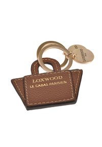 Porte-clés en cuir brun en forme de sac fourre-tout, avec le texte doré "LOXWOOD," et une bague en métal doré avec une étiquette attachée.