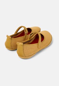 Zapatos acolchados amarillos con parte superior de malla, punta curvada y cinturón para el tobillo. Forro interior rojo y suela de goma plana para mayor comodidad.