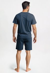 Donkerblauw katoenen t-shirt en korte broek set. T-shirt heeft een ronde hals en korte mouwen. De korte broek komt tot halverwege de dijen en heeft een elastische tailleband. Blote voeten.