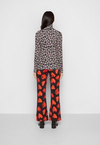 Svart topp med färgglad hjärtpattern; långärmade, hög krage. Röda hjärtformade utsvängda byxor. Svarta skor med tjock sula.