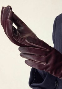 Burgunderfarbene Lederhandschuhe mit einer weichen Textur, ausgestattet mit fünf Fingern und einem enganliegenden Design, auf einem hellen Hintergrund präsentiert.