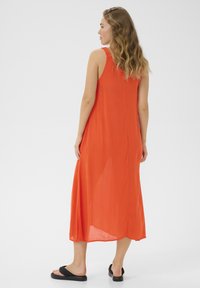 Maxiklänning i livfull orange tyg med en flödande design, axelremmar och sidslitsar. Matchad med svarta sandaler.