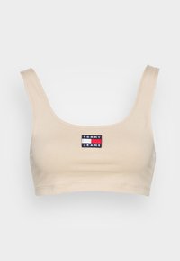 Bralette in cotone beige con scollatura a forma di ciotola e spalline larghe, caratterizzato da un piccolo patch ricamato con il logo Tommy Jeans al centro.