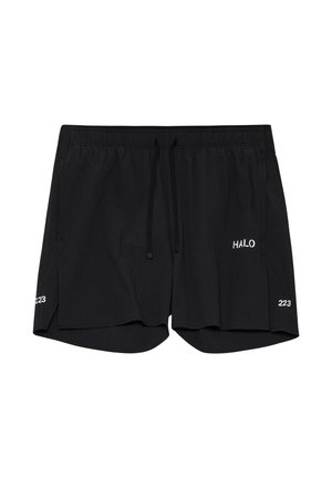 Mand står vendt fremad iført sort t-shirt med lille hvid tekst, sorte shorts, hvide sokker og grå sneakers på hvid baggrund.