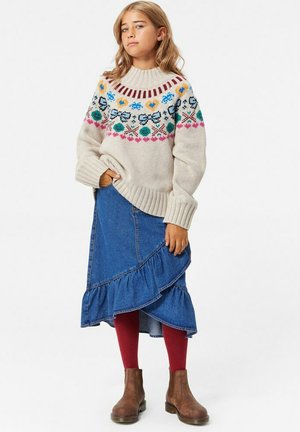 Stickad tröja med flerfärgade blommönster, krämfärgad, ribbade ärmslut; denimbukser med volanger; vinröda strumpbyxor; bruna ankelboots.