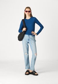 Μπλε πουκάμισο με μακριά μανίκια, ανοιχτόχρωμα τζιν με ελαφριά φθορά, μαύρες πλατφόρμες και μια υφασμάτινη μαύρη τσάντα ώμου; ροζ γυαλιά ηλίου ολοκληρώνουν το look.