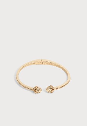 Bracelet manchette ouvert en or avec bande perlée texturée et extrémités rondes décoratives, présenté sur un fond clair uni.