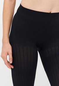 Schwarze Leggings mit geripptem Muster im unteren Bereich, glattem Stoff im oberen Bereich und einem elastischen Bund für eine sichere Passform.