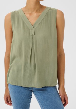 Blouse sans manches vert clair avec col en V et détail d'un seul bouton, portée avec un jean bleu.