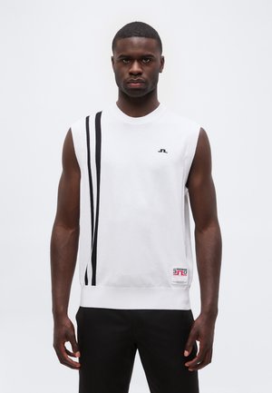 Homme portant un haut blanc sans manches avec deux bandes noires verticales et un petit logo sur la poitrine, associé à un pantalon noir, debout sur fond blanc.