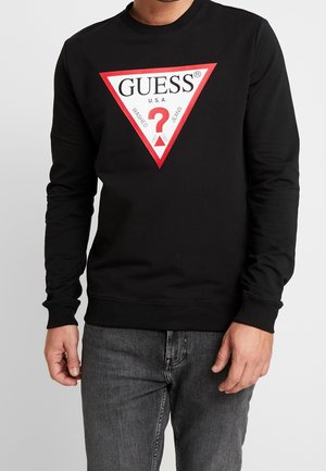 Sudadera negra hecha de algodón con escote redondo. Presenta una gran gráfica triangular roja y blanca con la palabra "GUESS?" en texto en negrita.