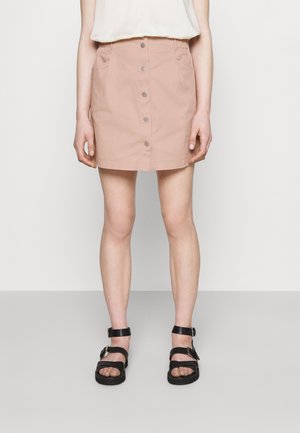 Světle růžová sukně se rovný střih, přední knoflíky a boční kapsy, spárovaná s černými sandály na pásky s nastavitelnými sponami.