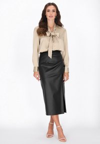 Beige silk bluse med en sløjfedetalje, parret med en sort pencilskørt i faux læder med en sideslids. Klare hæle med stropper fuldender looket.