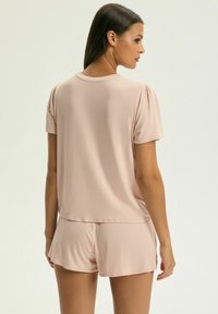 Krótki rękaw, jasnoróżowy zestaw odzieży domowej z luźnym topem z delikatnie bufiastymi rękawami oraz dopasowanymi szortami o miękkiej teksturze.