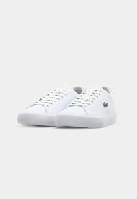 Balti sportiniai bateliai su lygiu odiniu paviršiumi, apvalia nosimi, baltais raišteliais, tekstūruotu guminio pado ir Lacoste logotipo akcentais šone.