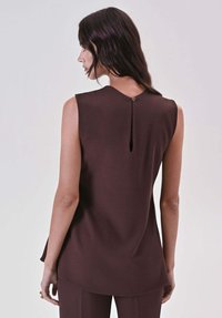 Top marrone senza maniche con scollo rotondo, caratterizzato da un dettaglio a goccia sulla schiena chiuso da un piccolo bottone. Tessuto liscio e vestibilità sagomata.