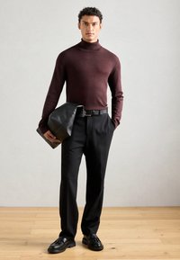 Bordeaux coltrui, zwarte op maat gemaakte broek, houdend een zwarte leren tas en zwarte veterschoenen. Zachte texturen, minimalistisch ontwerp.