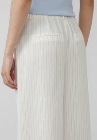 Pantalons blancs à rayures sur tissu avec une coupe décontractée, comportant deux poches arrière et une texture de tissu lisse. Les rayures sont d'un bleu clair contrastant.