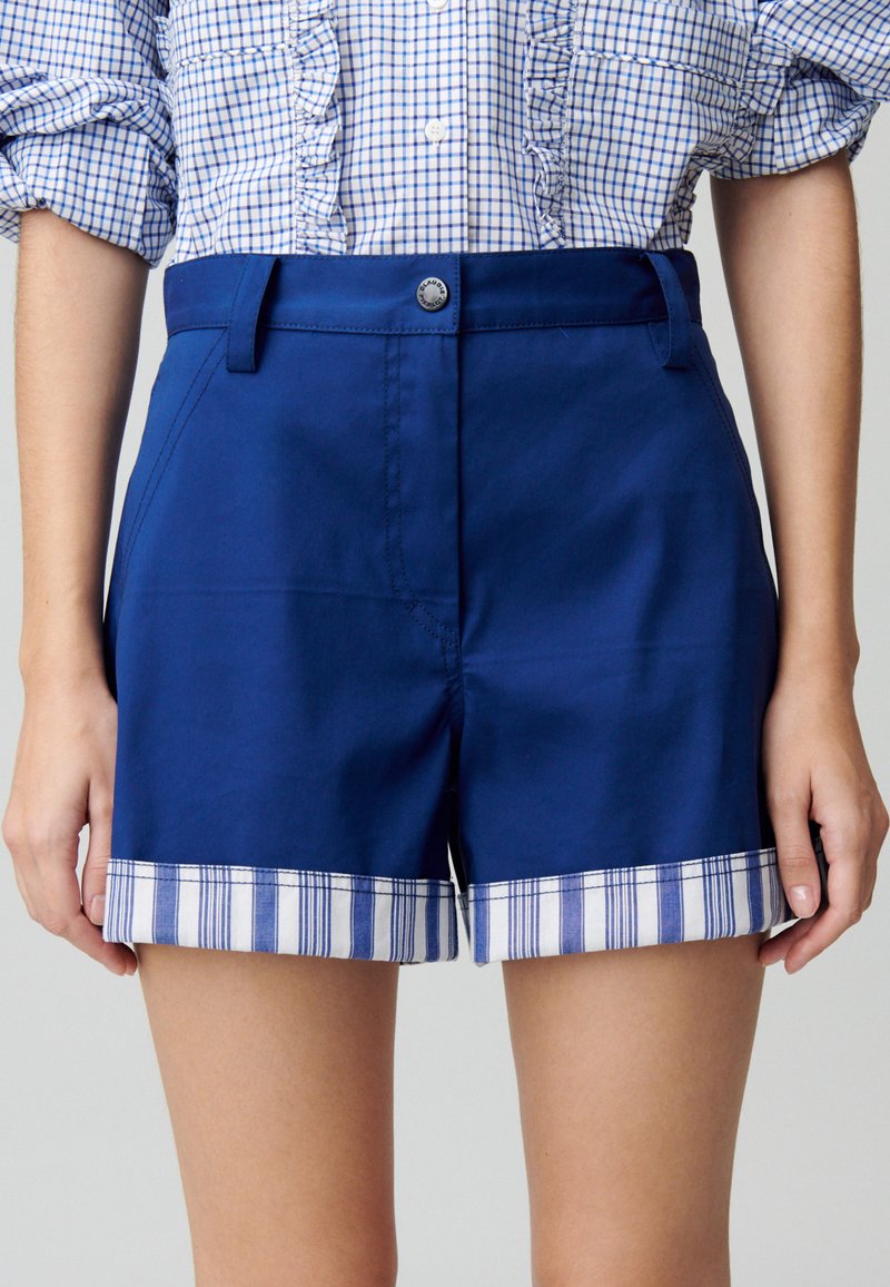 Shorts bleu marine avec un revers à motifs carreaux bleus et blancs. Fabriqués en tissu lisse, avec des poches avant et une fermeture à bouton.