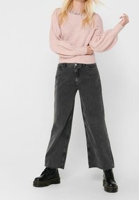 Mjuk rosa stickad tröja med ballongsärmar, kombinerad med högmidjade, vida svarta jeans och kraftiga svarta snörkängor.