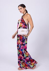Farverig blomster maxi kjole med halterneck design, lavet af letvægtsstof. En lille hvid taske med en guldlås holdes af modellen.