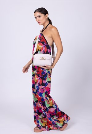 Maxi dress floreale colorato con design a collo halter, realizzato in tessuto leggero. La modella tiene una piccola borsa bianca con chiusura dorata.