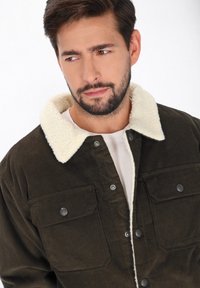 Sötétzöld cordúroy kabát, krémszínű, plüss gallérral, két mellsz zsebbel és patent gombos záródással.