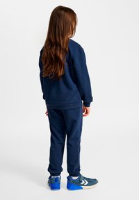 Mörkblå sweatshirt och matchande sweatpants i mjukt tyg, med ribbade muddar. Blå och grå träningsskor med vita detaljer och tjocka sulor.