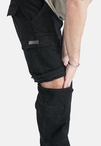 Sorte cargo bukser med en struktureret finish, der har lynlåse ved knæene og sidelommer. Stoffet viser holdbarhed og har en afslappet pasform.